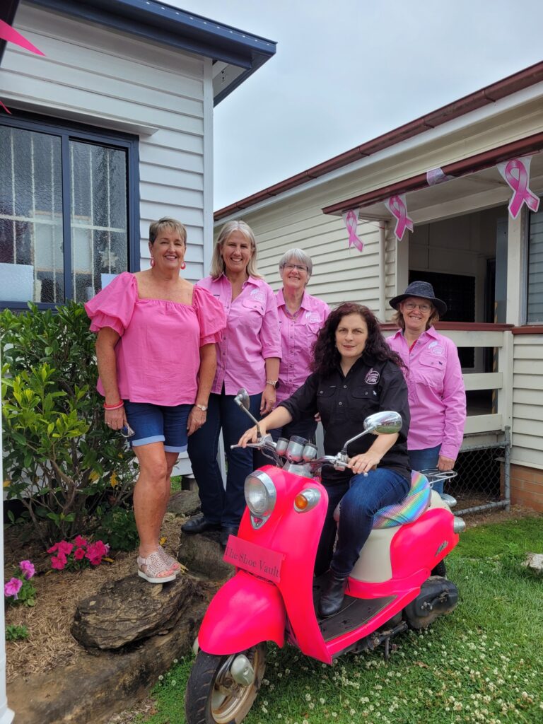 Turning Canungra Pink volunteers wearing pink shirts, with one sitting on a pink scooter.