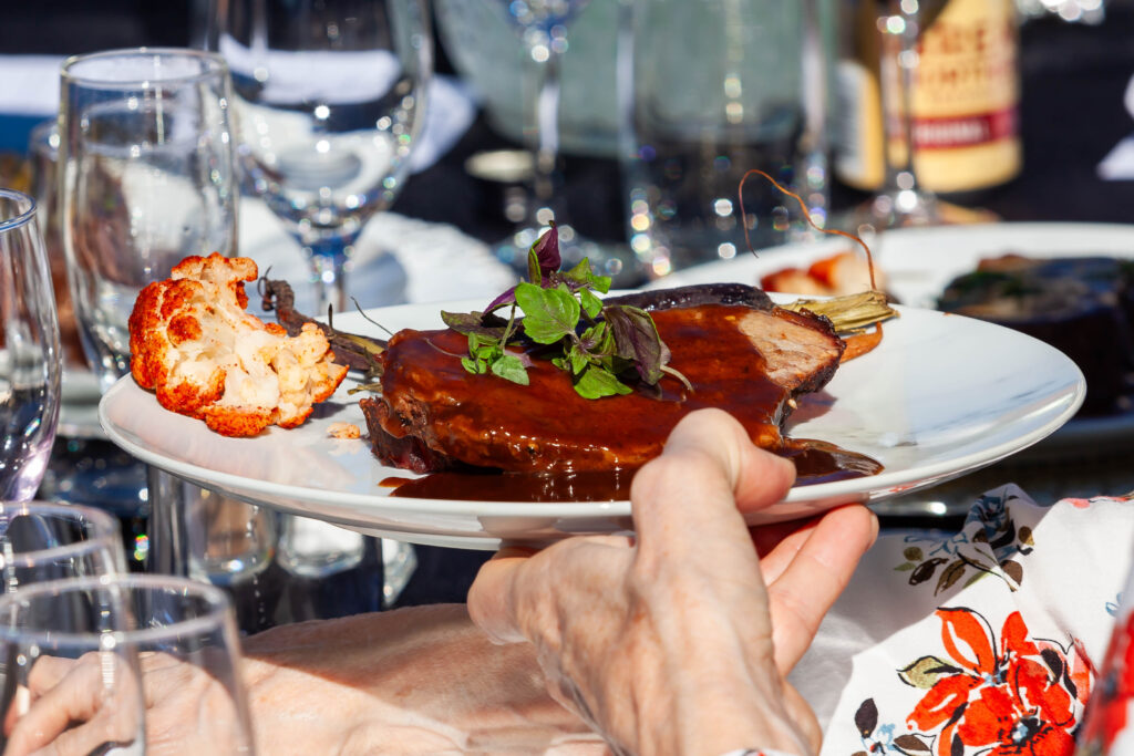 A hand holding a plate of Scenic Rim beef cooked to perfection, with tableware in the background.