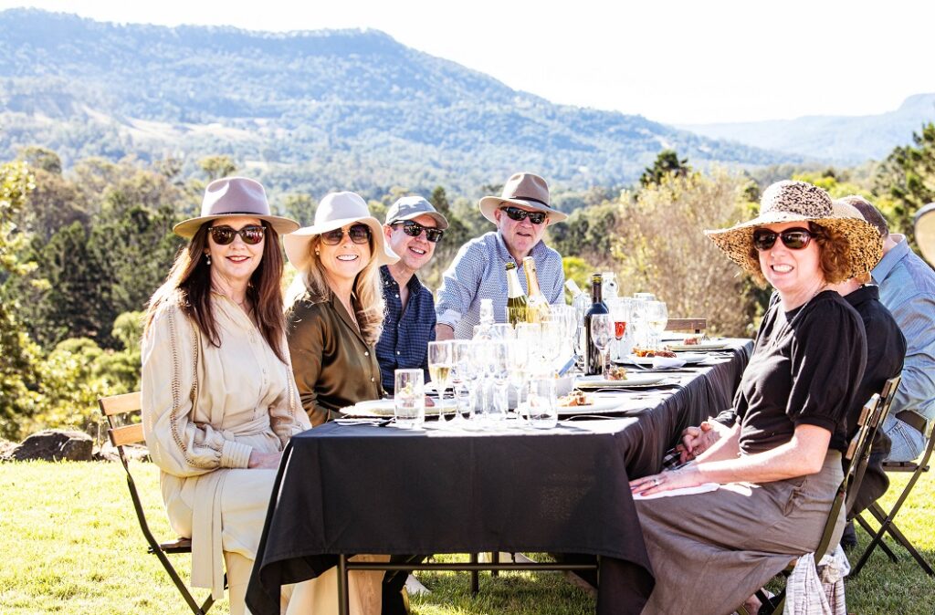 Group of people sitting at a table, enjoying the locally source food and wine at the Feast In the Valley lunch. Beautiful country scenery of Flying Fox Valley.