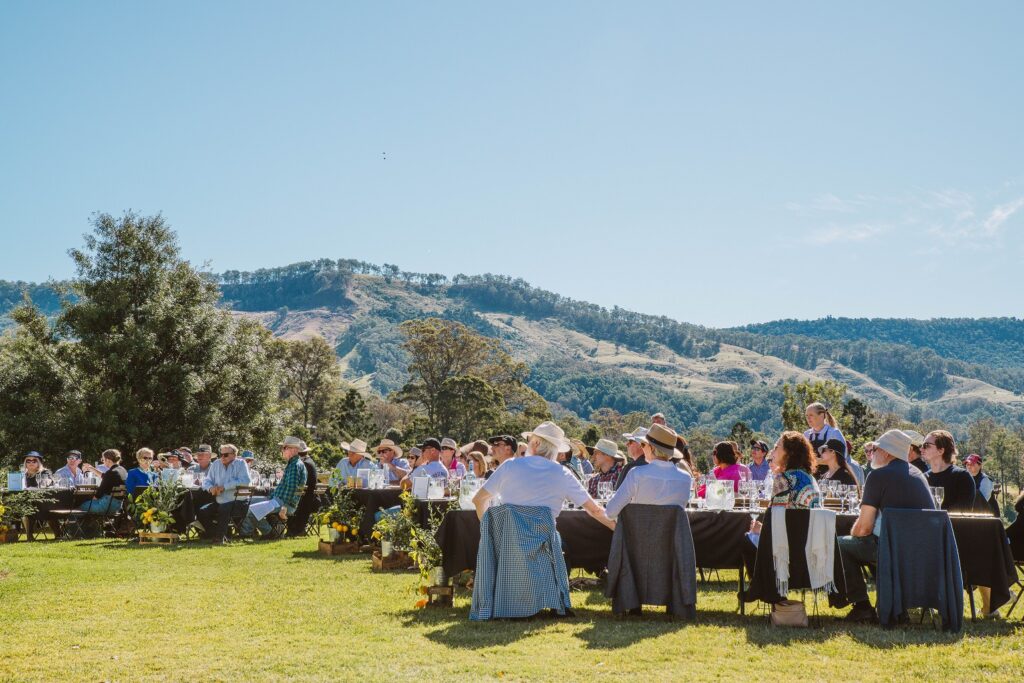 Group of people sitting at tables enjoying the beautiful sunny day at Feast in the Valley lunch and enjoying the host talking about Scenic Rim local produce.