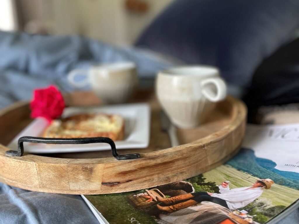 A tray with cups of coffee sitting on the bed with a magazine to read