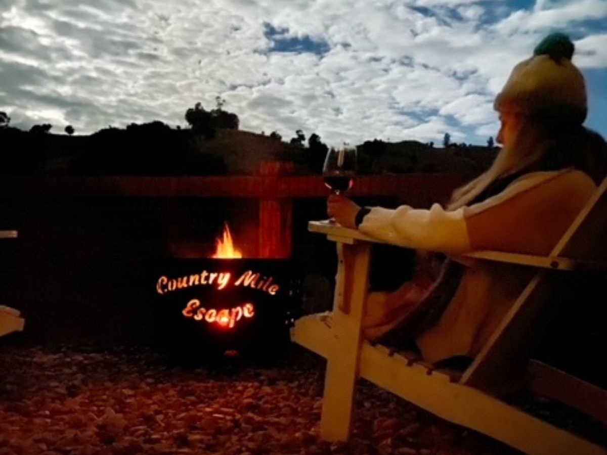 A guest sitting by a glowing fire pit under a twilight winter sky at Country Mile Escape