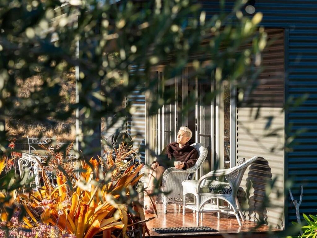 A lady sitting on the verandah of one of the romantic cottage at Country Mile Escape.