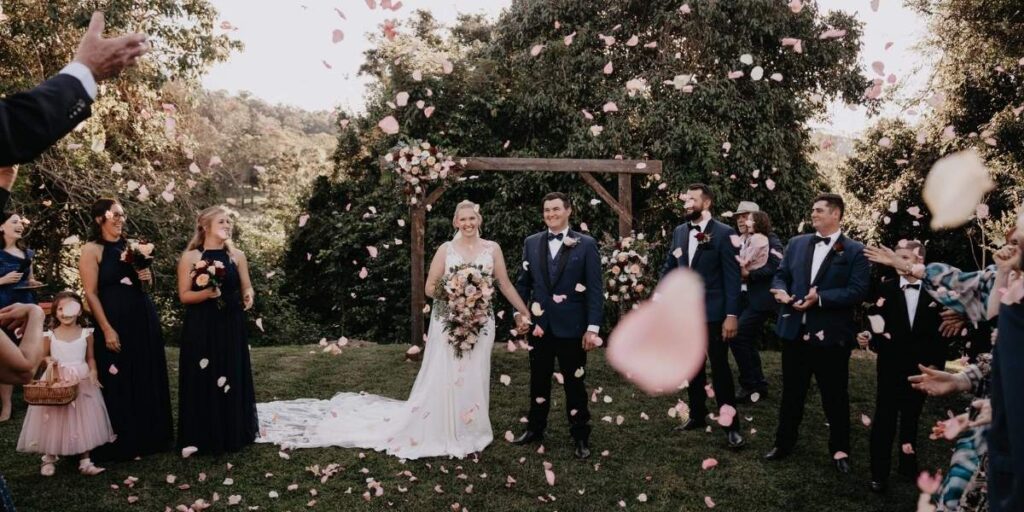Married Couple stand hand in hand with confetti flowing over them.